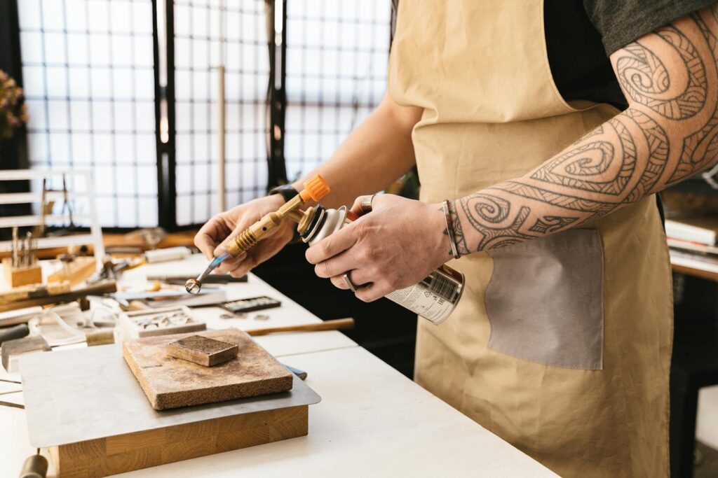 Close-up of a jeweler using a blowtorch on a work desk, highlighting tools and artisan skills.